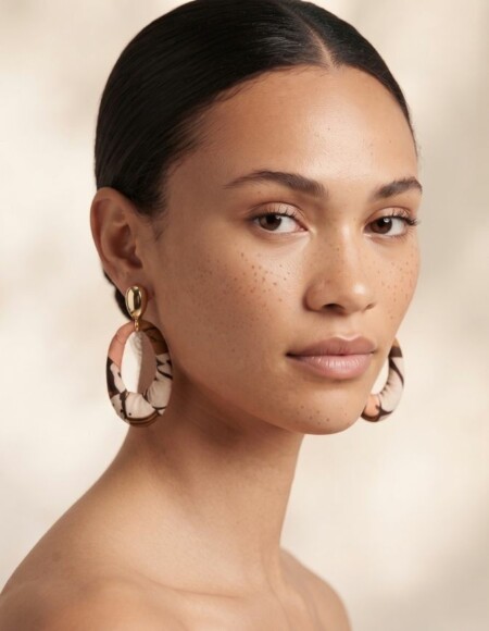Femme avec un chignon portant des boucles d'oreilles pendantes en acier inoxydable doré et tissu wax