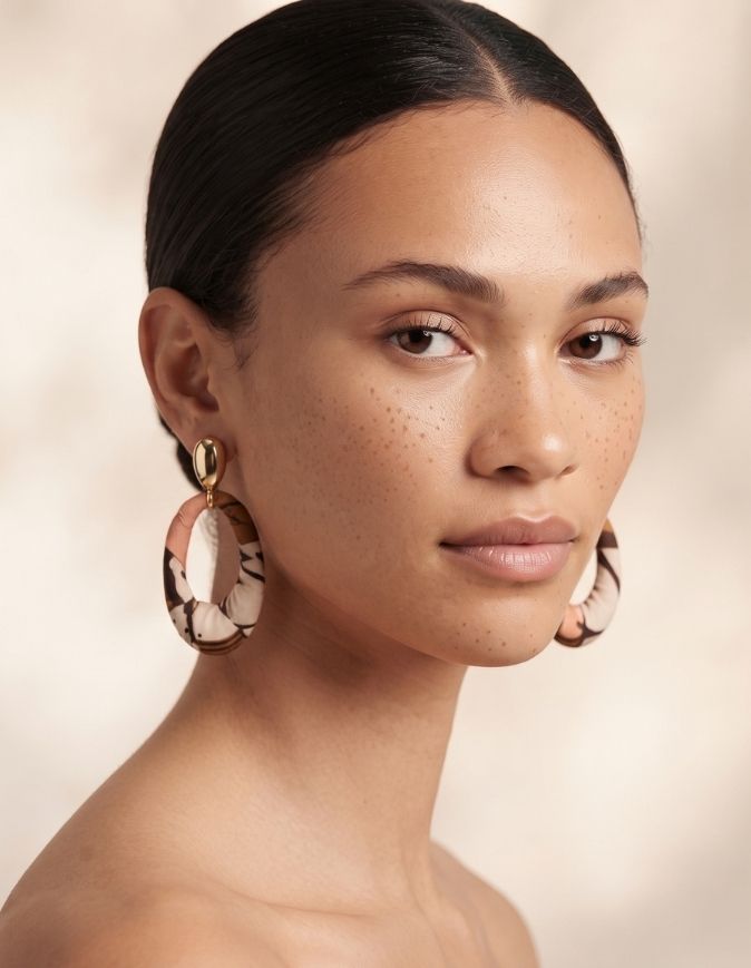 Femme avec un chignon portant des boucles d'oreilles pendantes en acier inoxydable doré et tissu wax